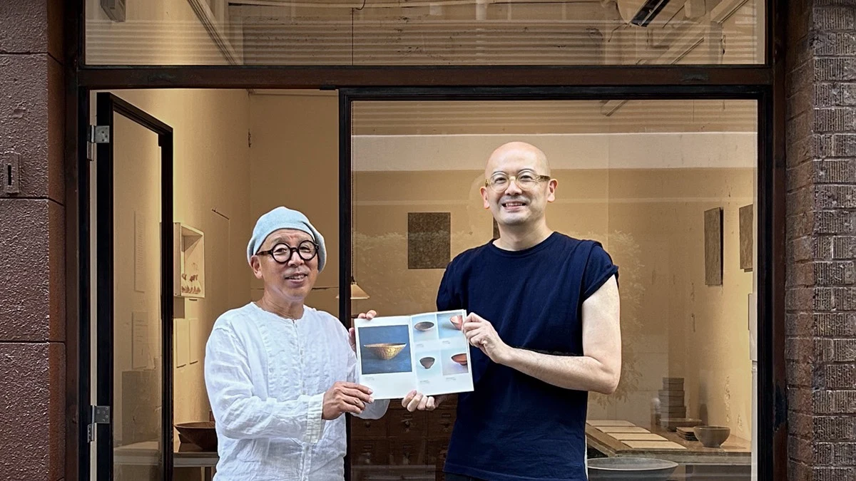 Yoshiyuki Morioka và Yoshifumi Yamamoto đứng trước cửa hiệu Morioka Shoten ở Tokyo, cùng cầm một cuốn sách mở