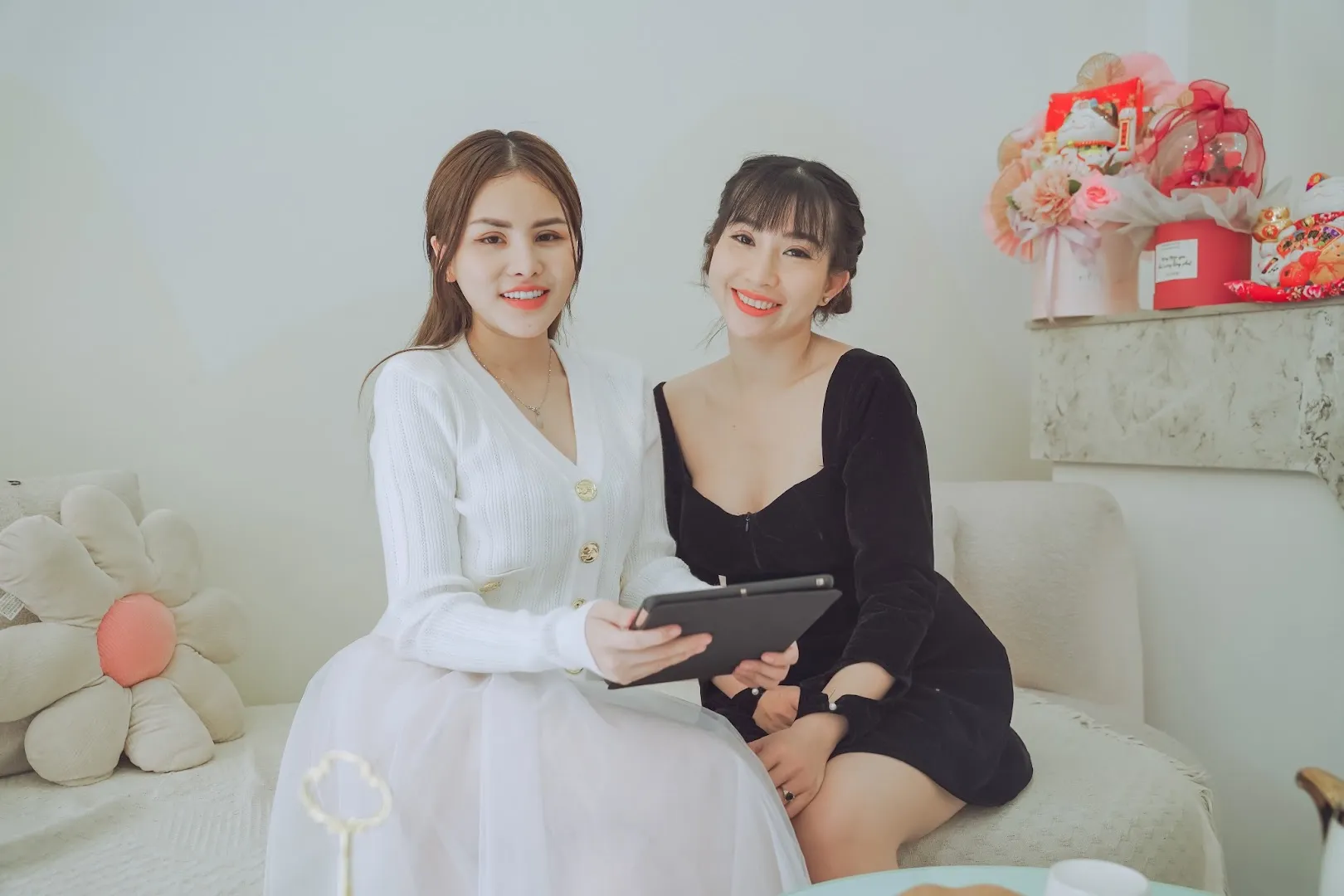 Hai người phụ nữ ngồi trên ghế sofa trong không gian spa, một người cầm máy tính bảng.