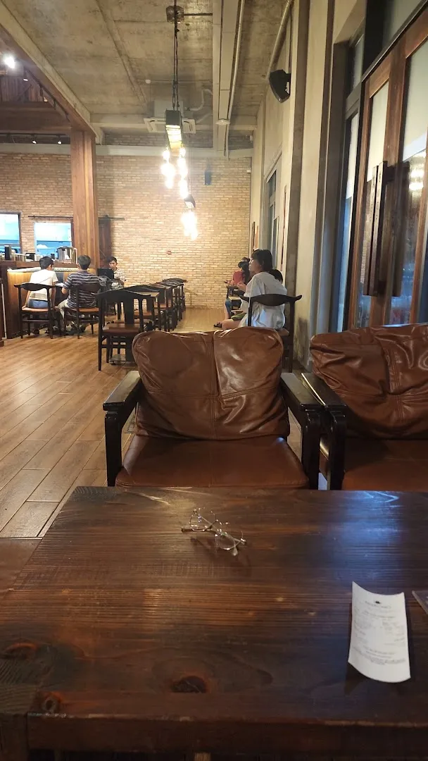 Không gian bên trong quán cà phê với bàn ghế gỗ, ghế bành da và ánh đèn ấm áp.