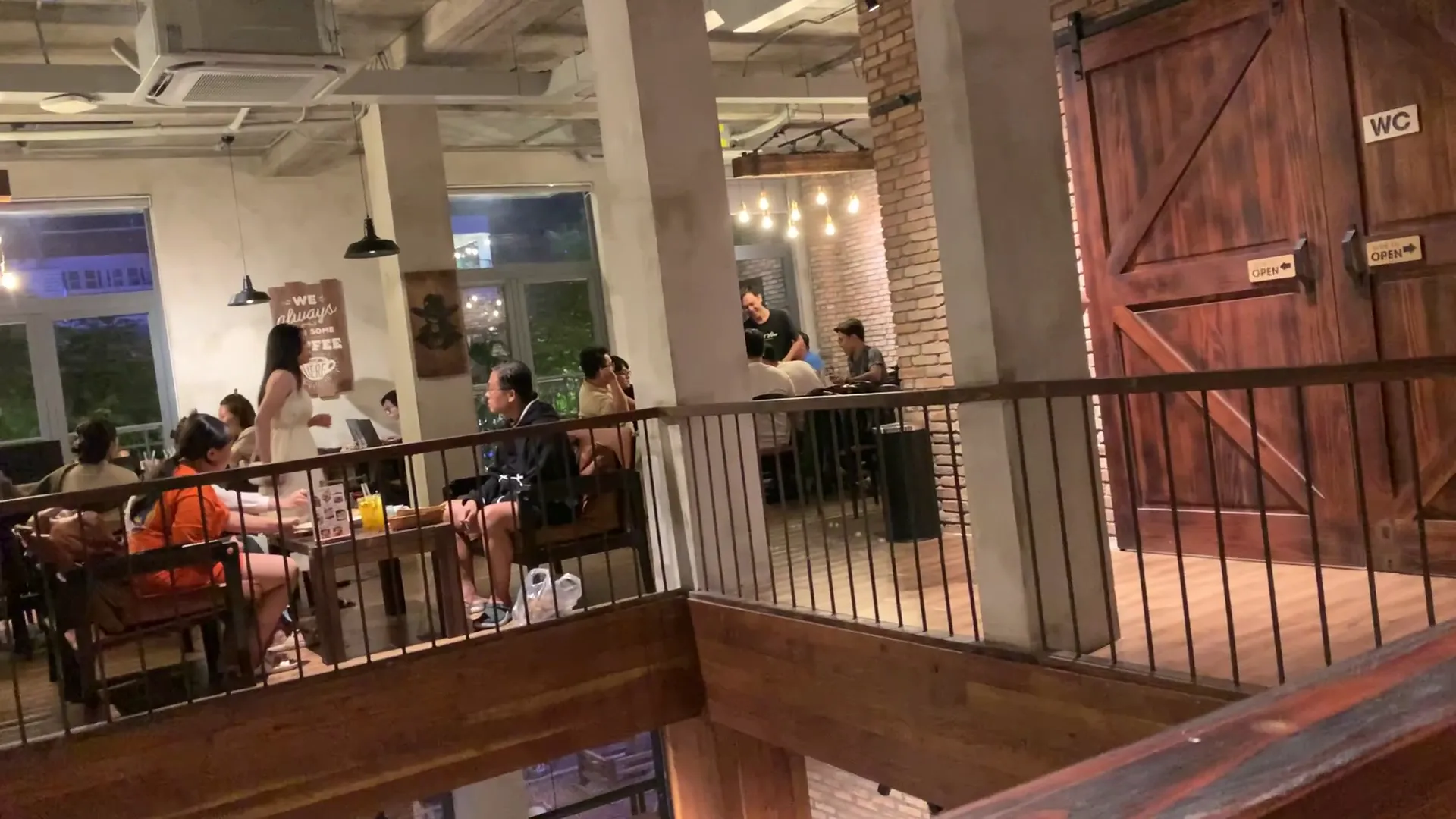 Không gian nội thất quán cà phê với bàn ghế, ánh đèn ấm và khách ngồi thưởng thức đồ uống.