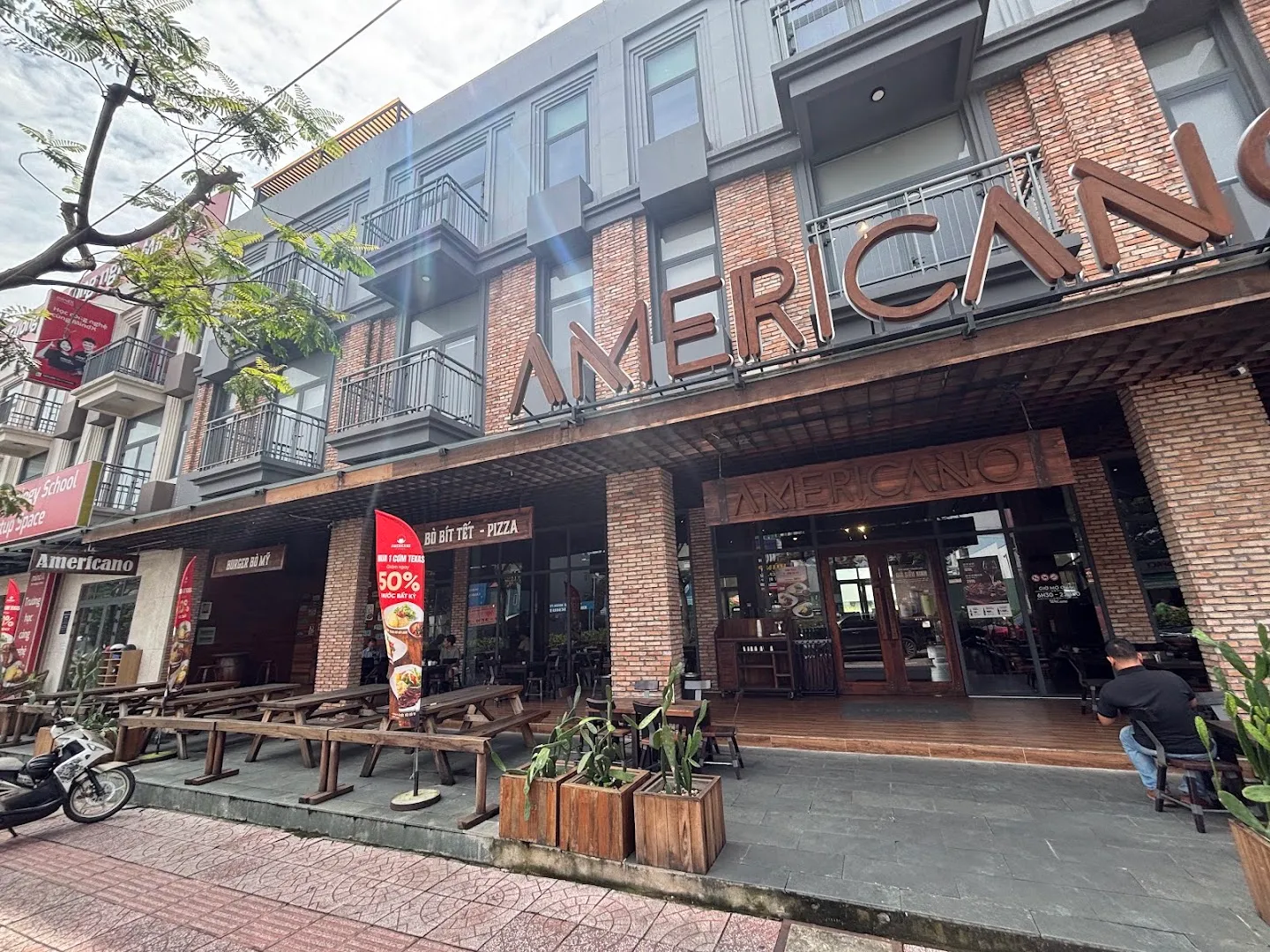 Mặt tiền quán AMERICANO với bảng hiệu rõ ràng, cửa ra vào và khu bàn ghế ngoài trời.