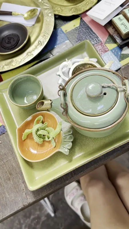 Bộ ấm trà gốm xanh kèm tách và đĩa bánh mứt trên khay.