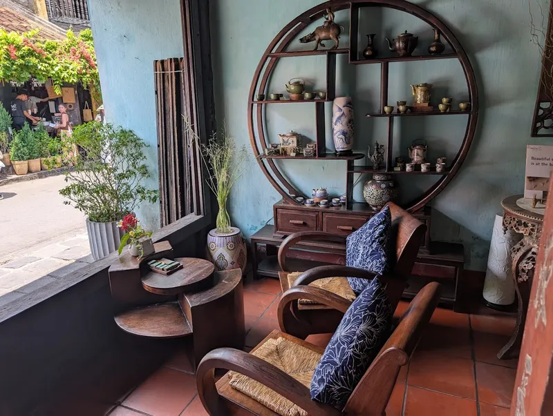 Không gian phòng trà ấm cúng với ghế gỗ, bàn trà và kệ trưng bày ấm chén.