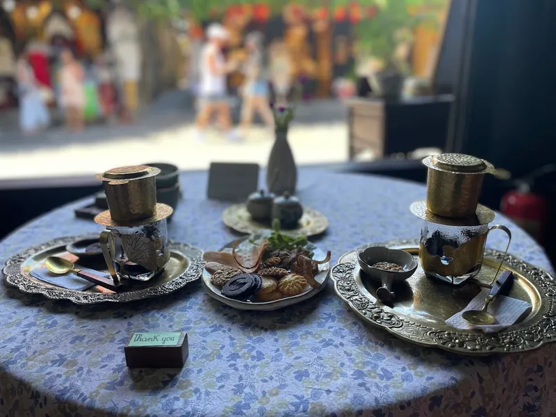 Bàn trà với hai phin cà phê, bánh ngọt và bộ ấm chén trang trí.