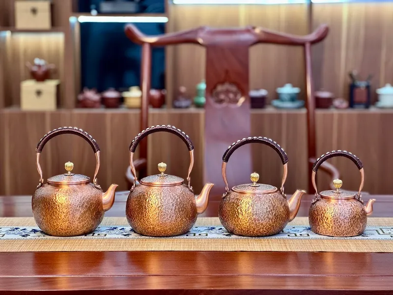 Bộ ấm đun trà bằng kim loại với quai cầm cong, được trưng bày trên kệ.