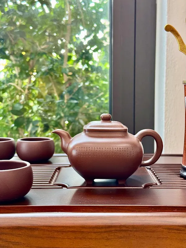 Ấm trà gốm và các chén trà đặt trên khay trà bằng gỗ.