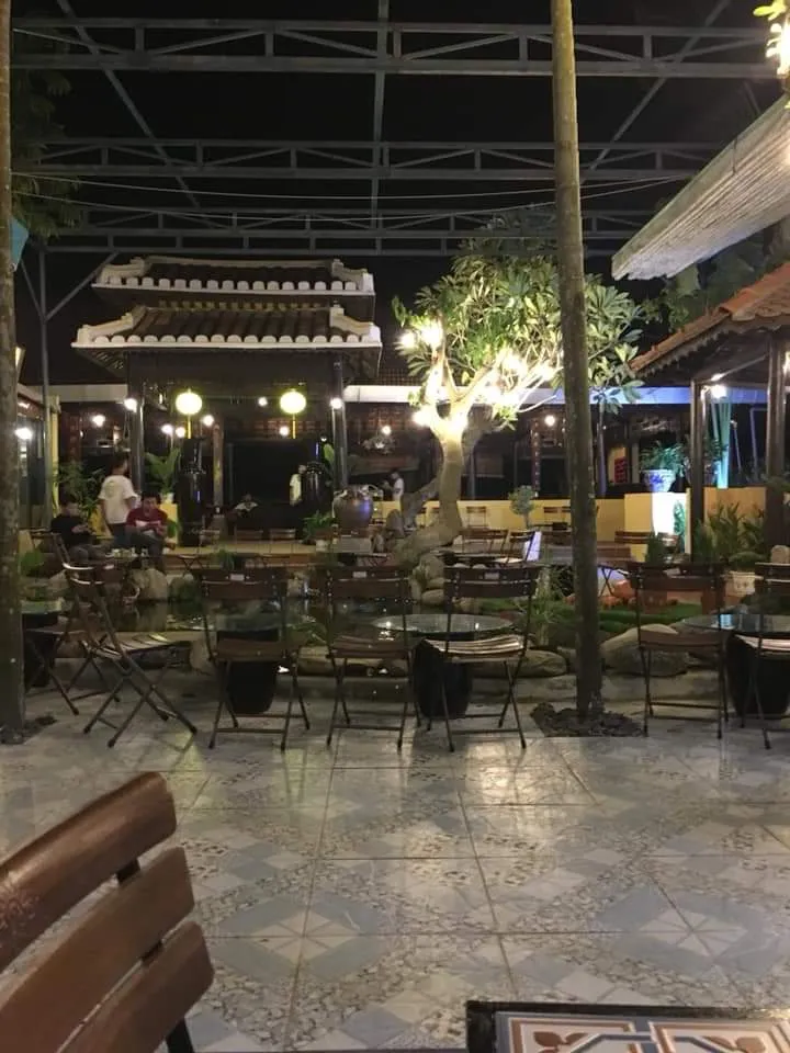 Không gian sân vườn buổi tối với bàn ghế ngoài trời và ánh đèn ấm cúng.