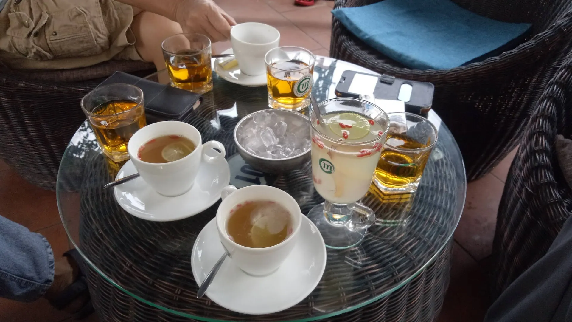 Bàn cà phê với nhiều tách đồ uống và ghế mây xung quanh