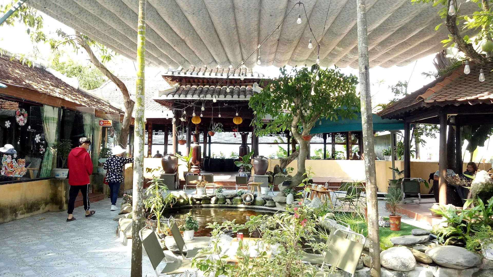 Không gian sân vườn với hồ cá, cây xanh và bàn ghế ngoài trời.