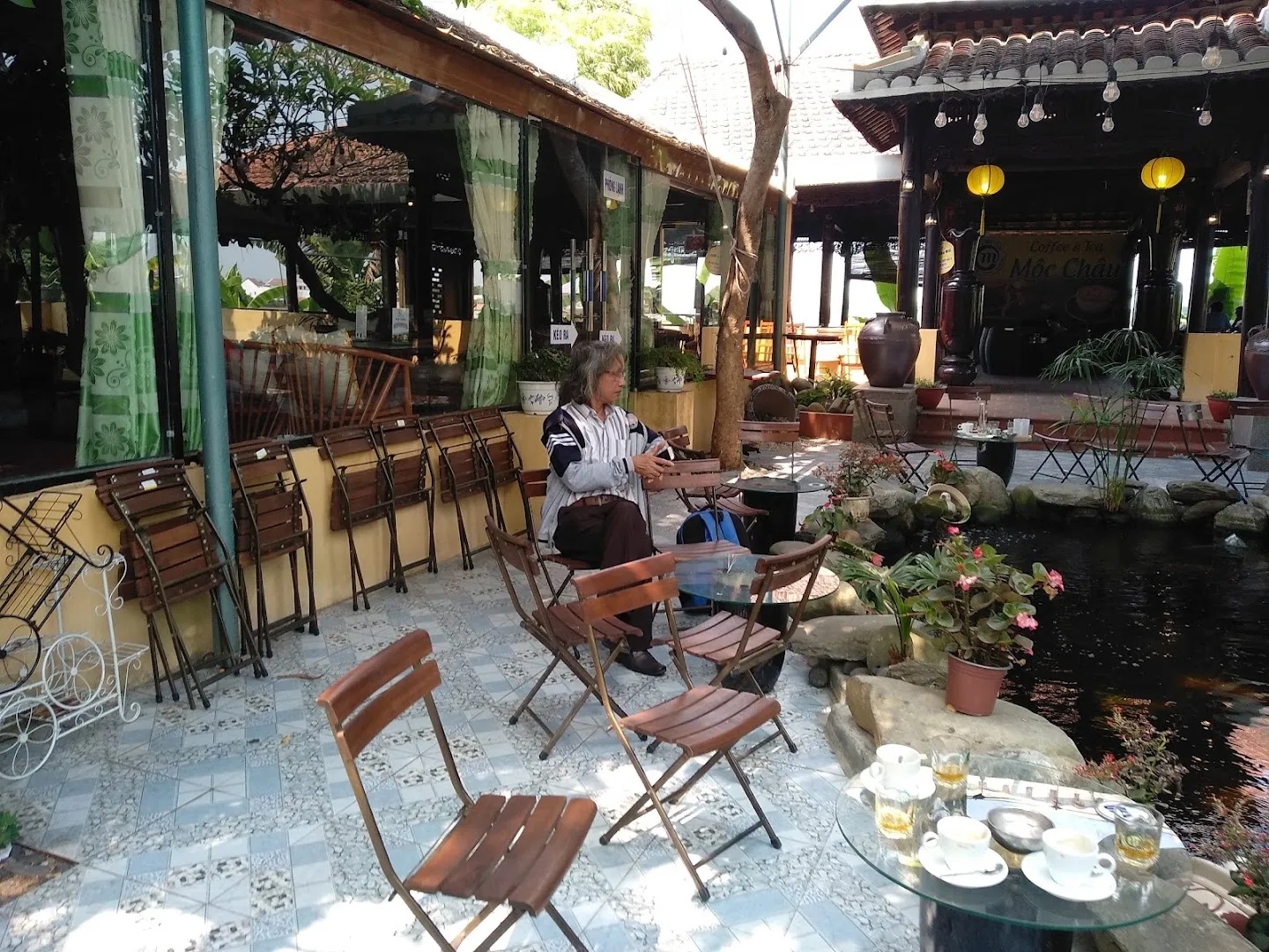 Không gian sân vườn với bàn ghế ngoài trời, hồ cá và đèn lồng trang trí.