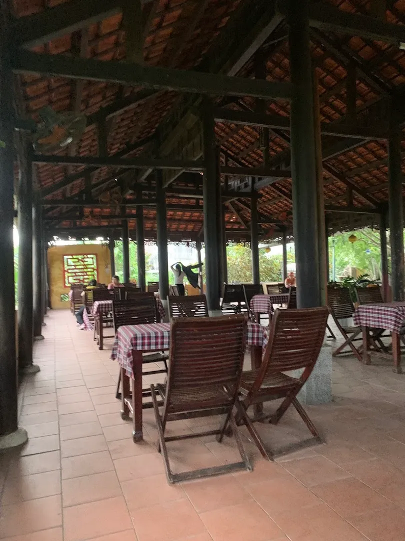 Không gian quán cà phê với mái ngói, bàn ghế gỗ và khu vực ngồi thoáng đãng.
