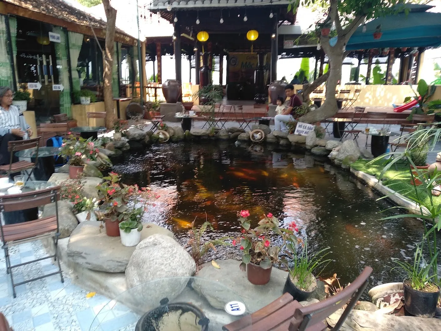 Không gian sân vườn của quán với hồ cá, cây xanh và khu vực bàn ghế ngoài trời.