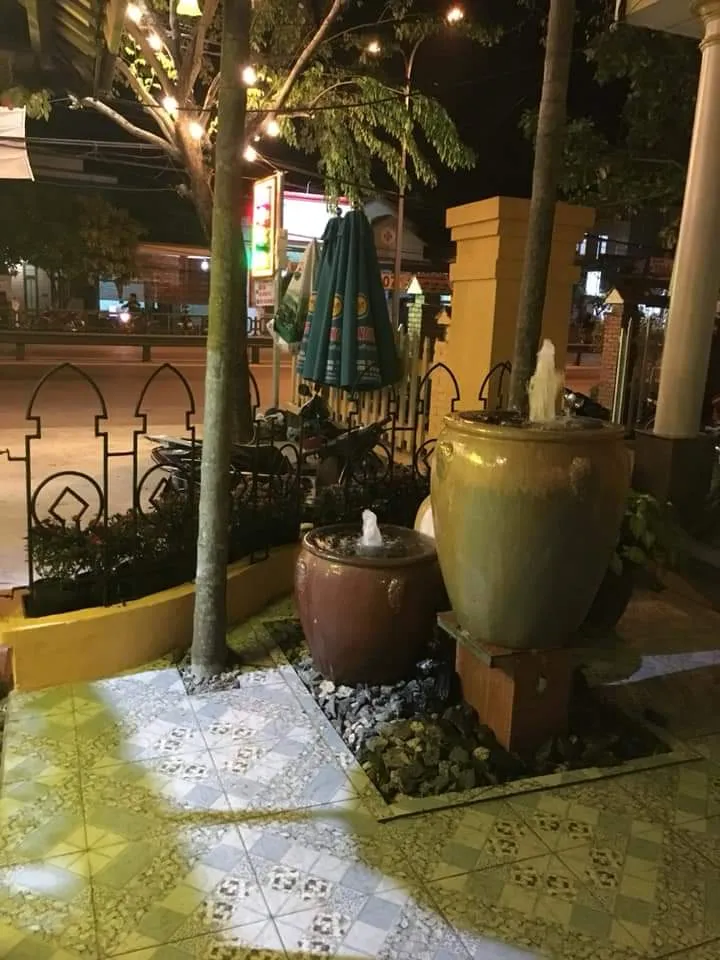 Góc sân ngoài trời với cây xanh, đèn trang trí, ô dù và tiểu cảnh chum nước.