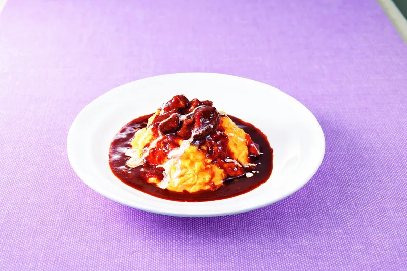 Món trứng omurice phủ sốt nâu và thịt hầm trên đĩa trắng.