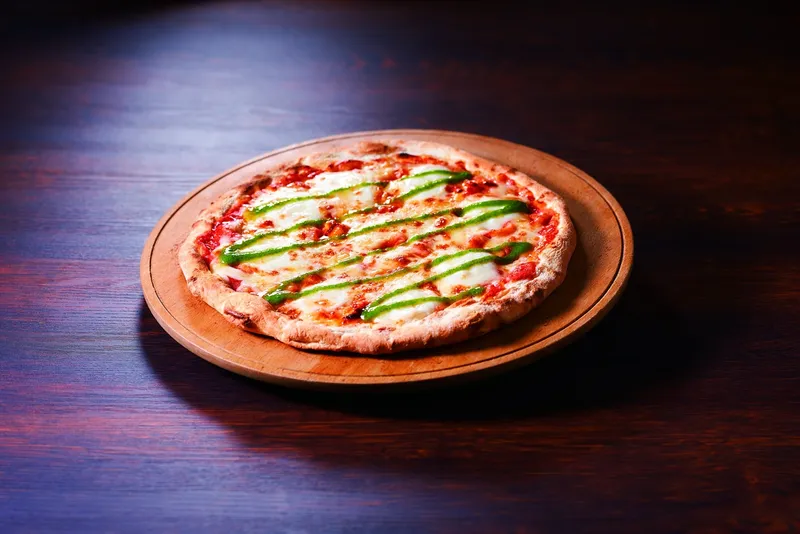 Pizza phô mai phủ sốt cà chua và ớt xanh trên đĩa gỗ.
