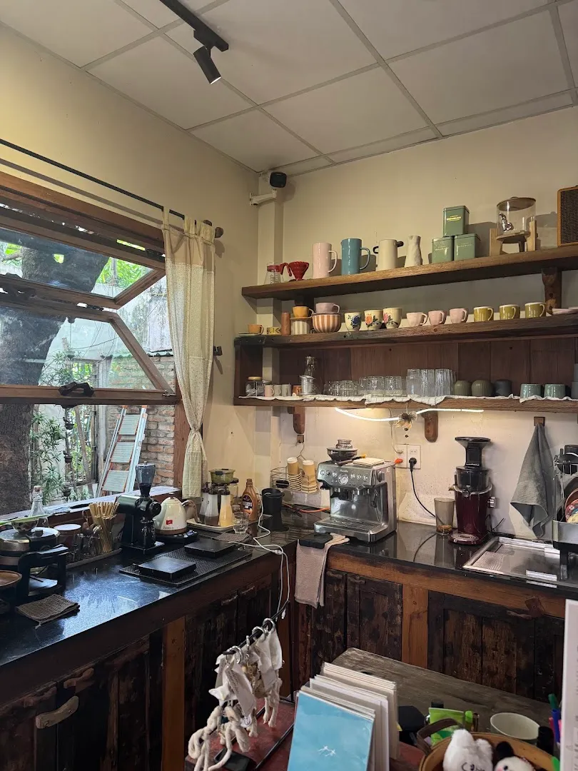 Quầy pha chế với máy espresso, dụng cụ pha cà phê và kệ đầy cốc gốm.