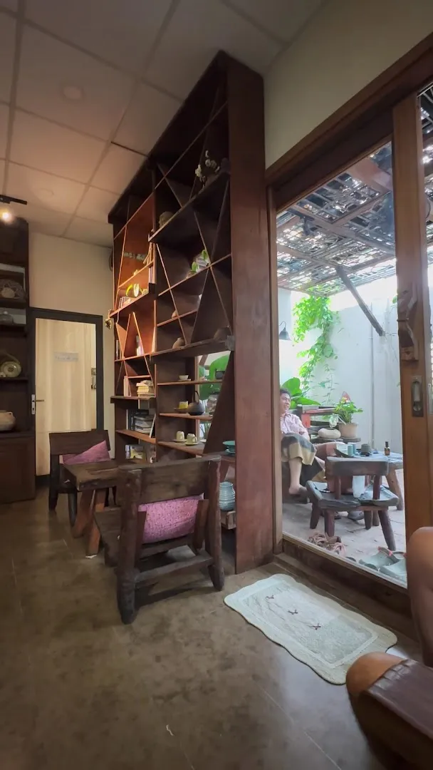 Không gian quán với kệ gỗ, bàn ghế và khu vực sân trong nhiều cây xanh.