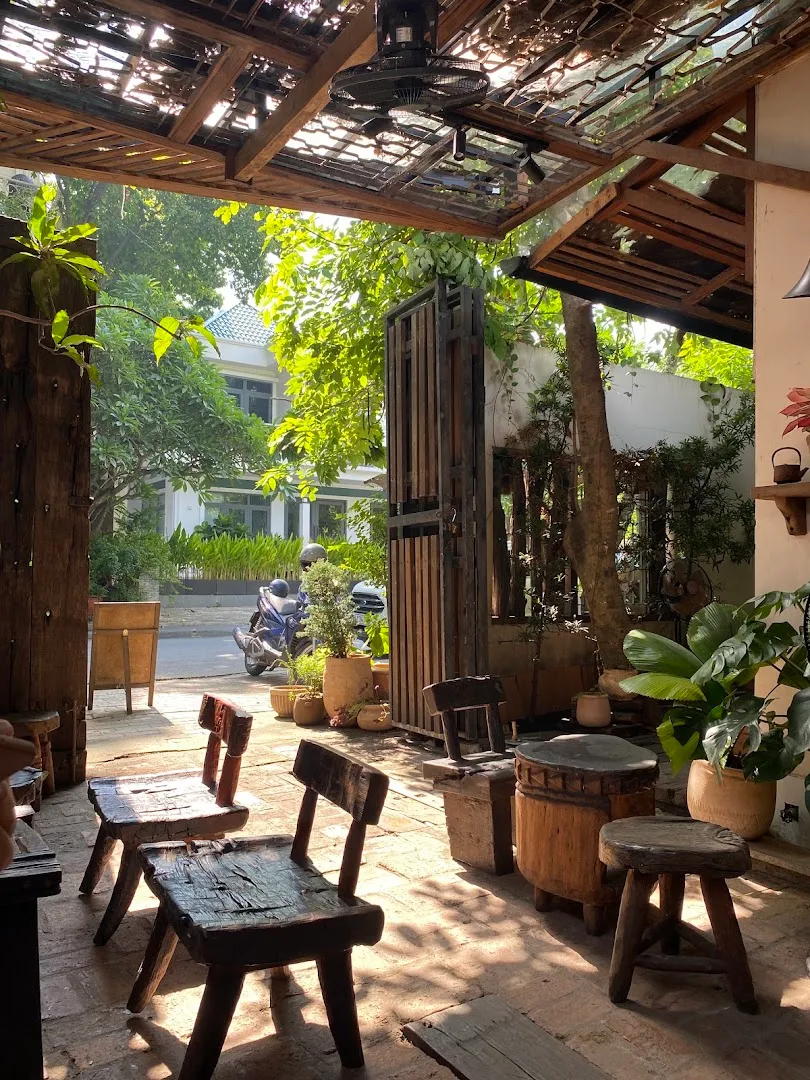 Không gian sân vườn với bàn ghế gỗ mộc mạc và nhiều cây xanh.