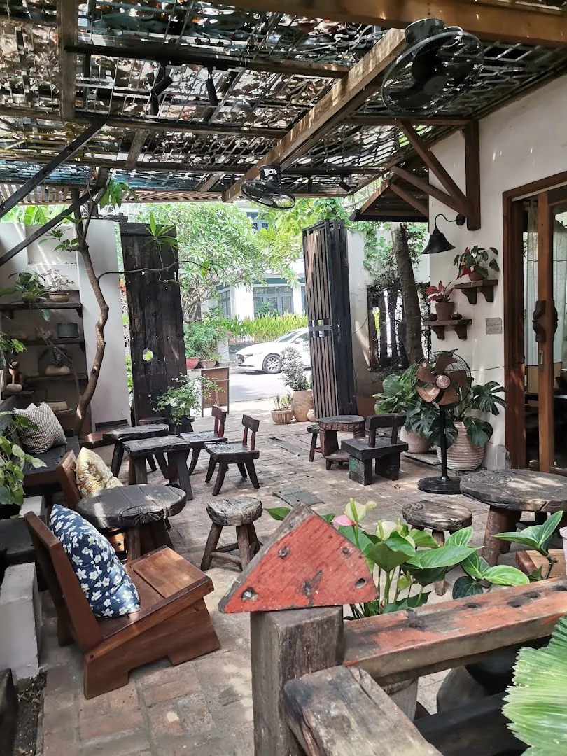 Không gian sân vườn với bàn ghế gỗ, cây xanh và mái che độc đáo.