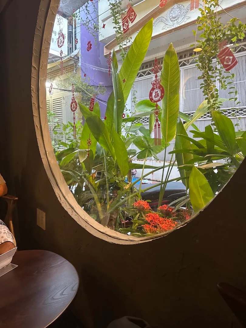 Góc không gian thư giãn với cửa sổ tròn, cây xanh và hoa trang trí.