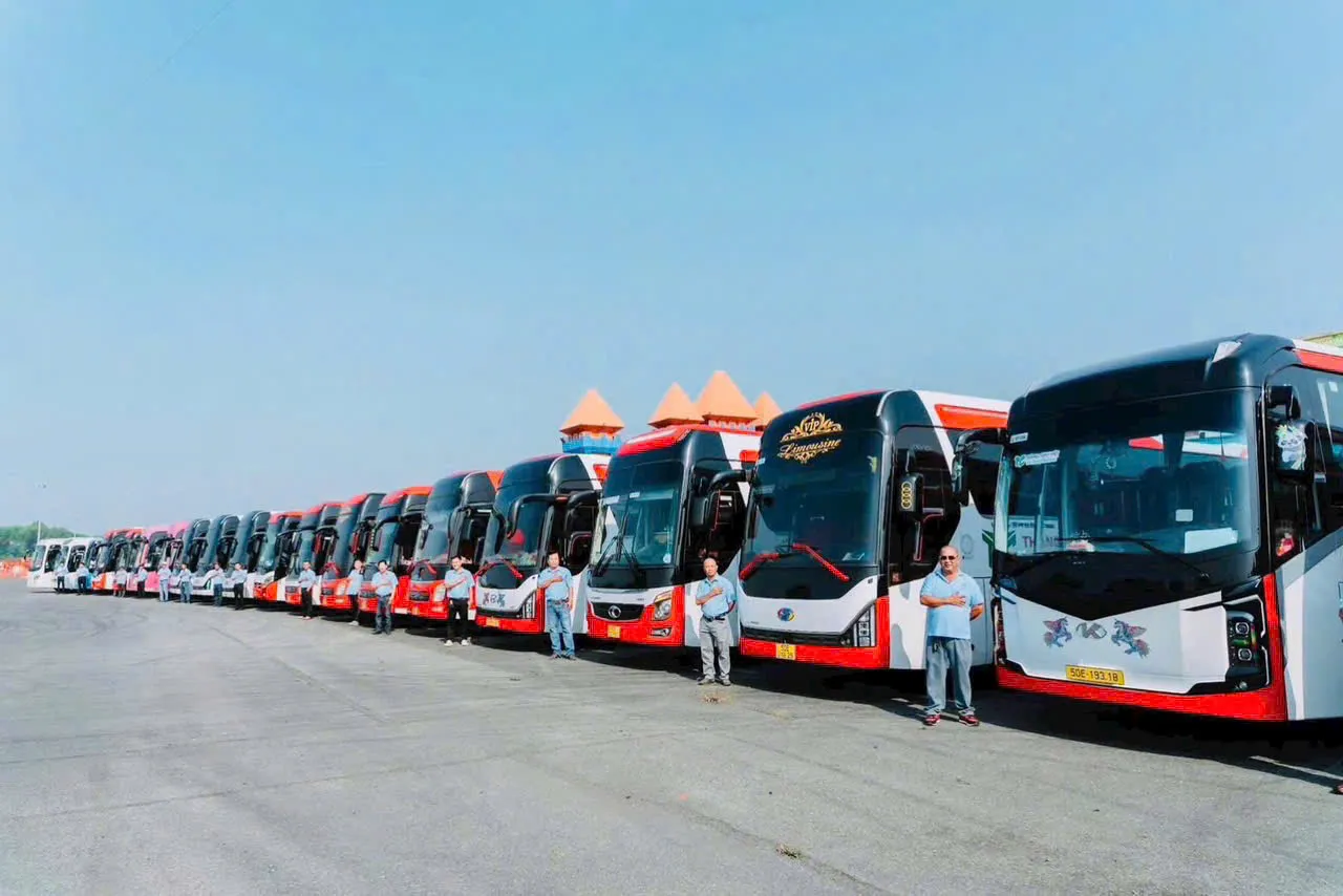 Đội xe khách cỡ lớn xếp hàng tại bãi đỗ, cùng các tài xế đứng phía trước.