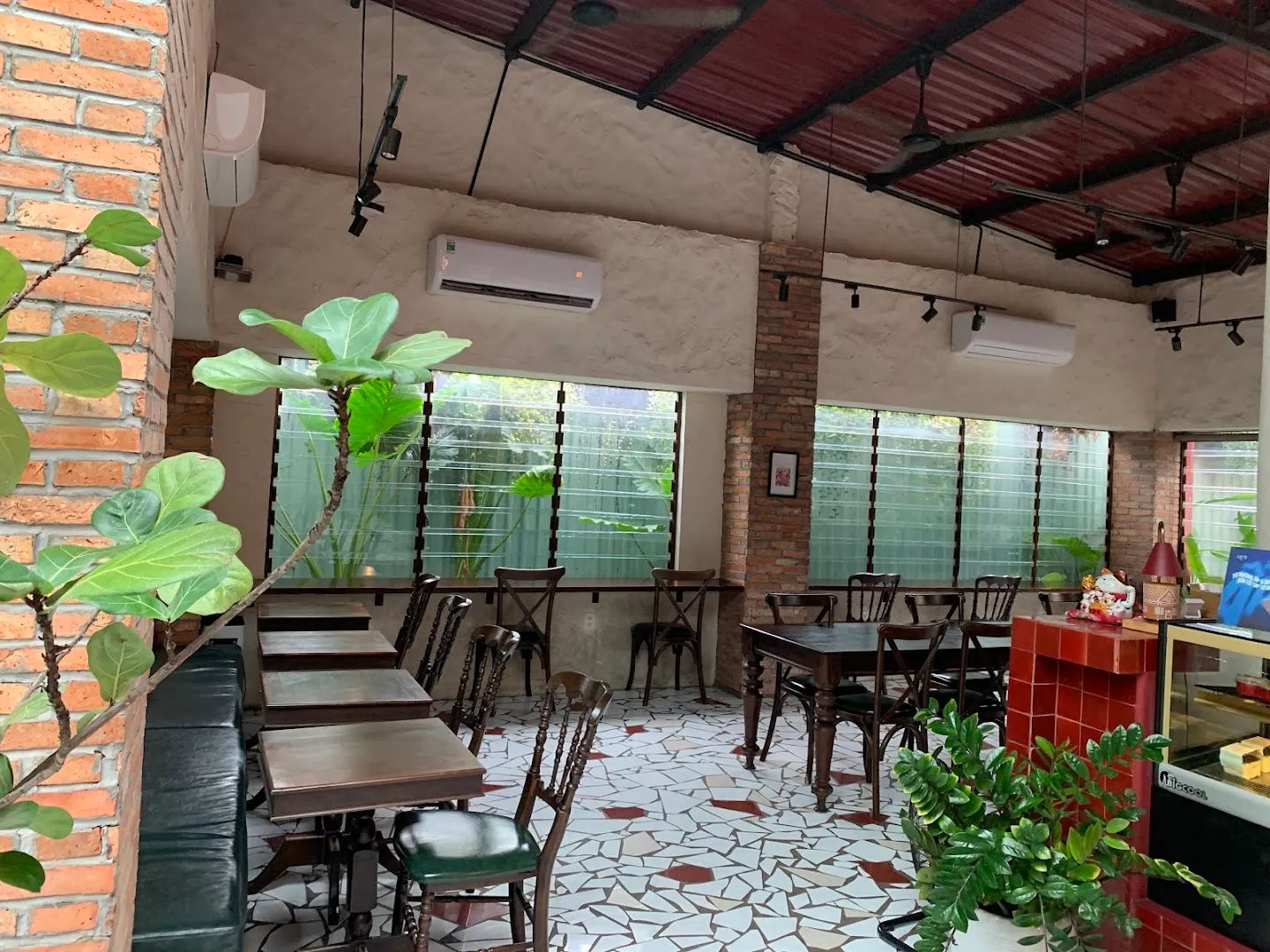 Không gian bên trong quán với bàn ghế gỗ, tường gạch và nhiều cây xanh.