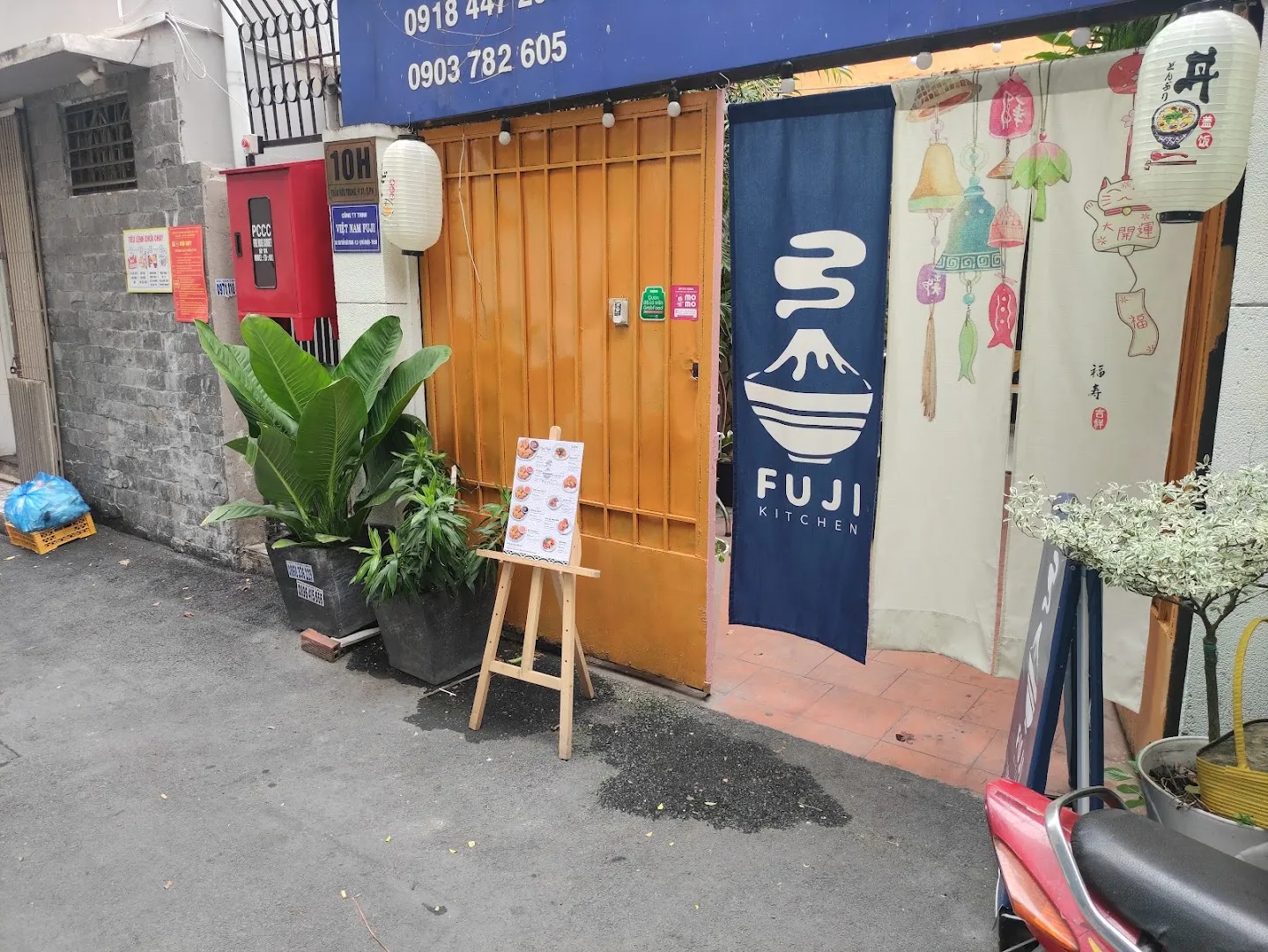 Mặt tiền Fuji Kitchen với biển hiệu, rèm cửa phong cách Nhật và bảng món đặt trước lối vào.