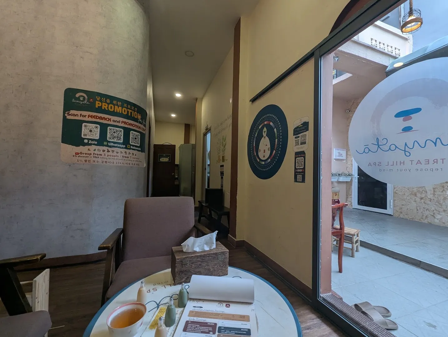 Khu vực tiếp khách với ghế ngồi, bàn trà và bảng khuyến mãi của spa.
