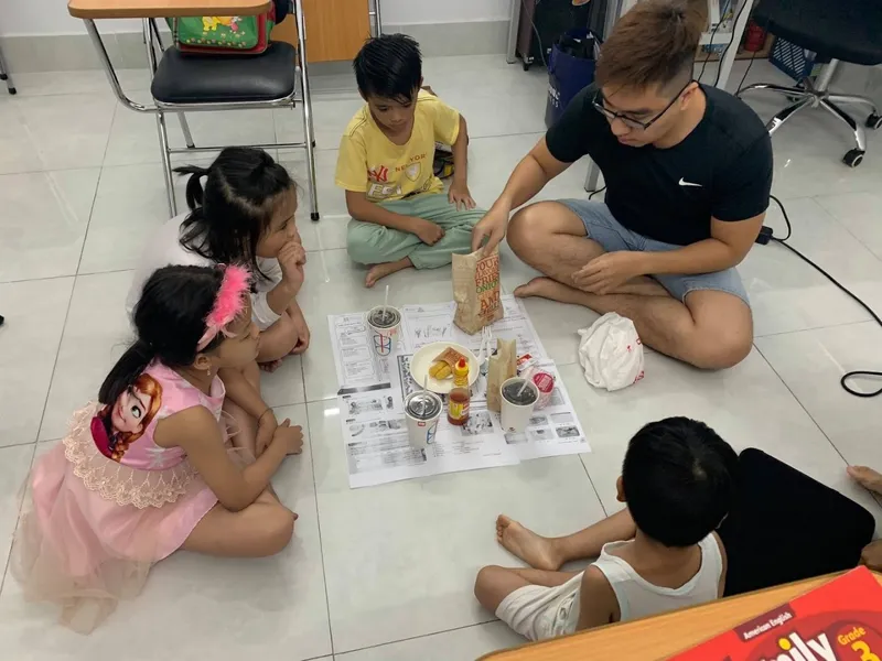 Một người lớn ngồi cùng các em nhỏ trong không gian học tập.