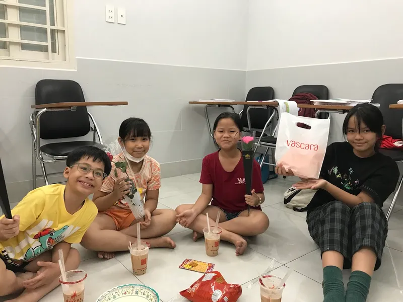 Một nhóm người ngồi trong phòng học, phía sau có bàn ghế học viên.