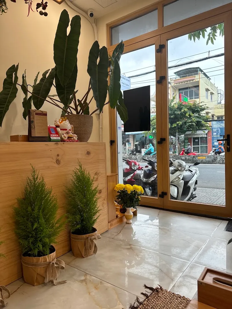 Không gian sảnh đón khách với quầy gỗ, cây xanh và cửa kính phía trước.