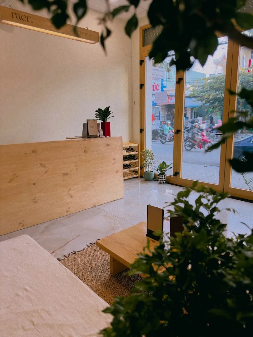 Không gian sảnh đón khách với quầy lễ tân bằng gỗ, cây xanh và cửa kính lớn.