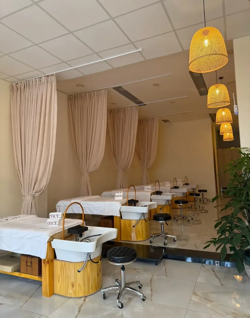 Không gian gội đầu thư giãn với các giường gội riêng biệt, rèm ngăn cách và ánh đèn ấm áp.