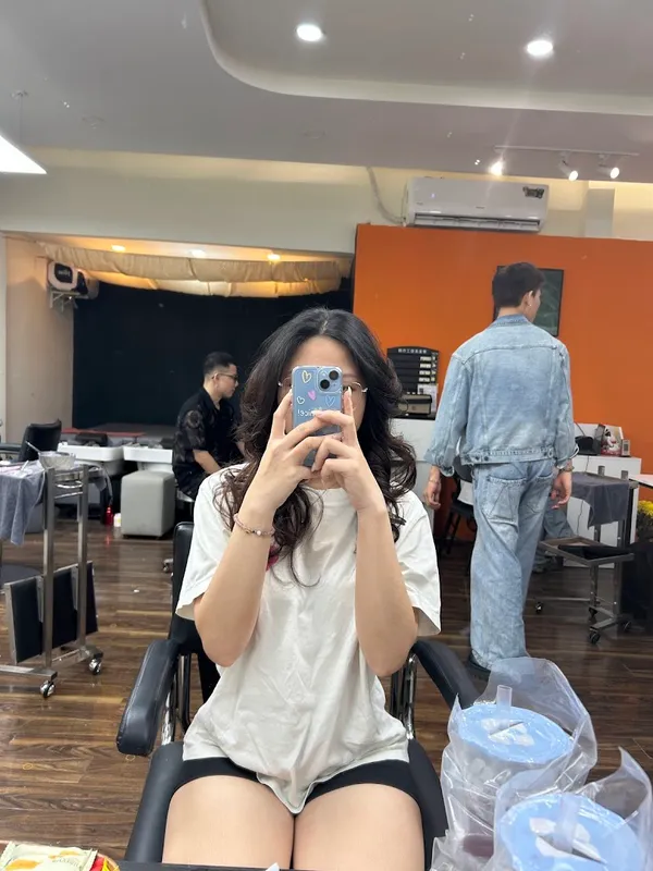 Không gian bên trong salon tóc với ghế làm tóc, xe dụng cụ và khách đang ngồi trước gương.