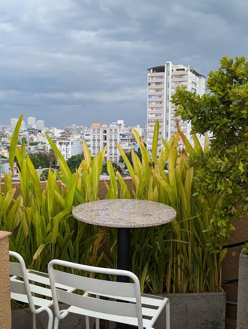 Góc bàn ghế ngoài trời giữa cây xanh, nhìn ra khung cảnh thành phố.