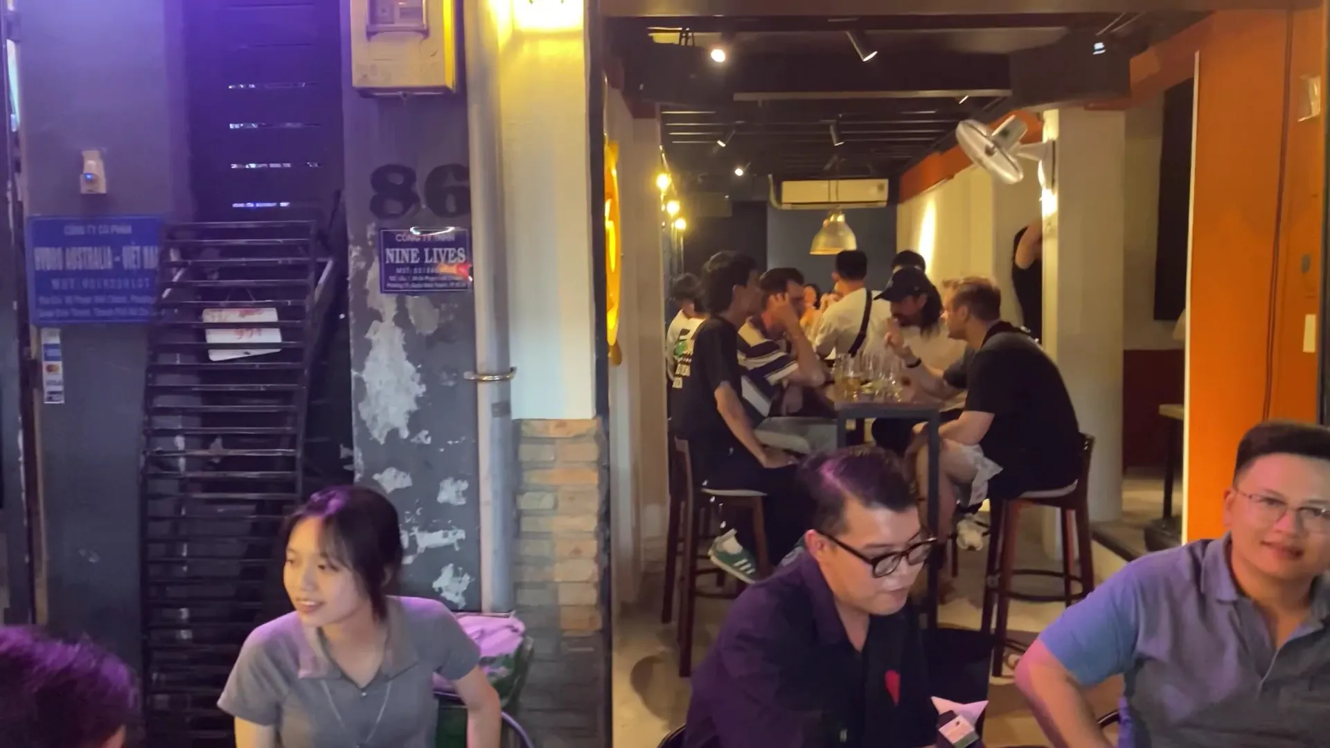 Không gian bên trong quán bar với bàn ghế cao và khách đang thưởng thức đồ uống.