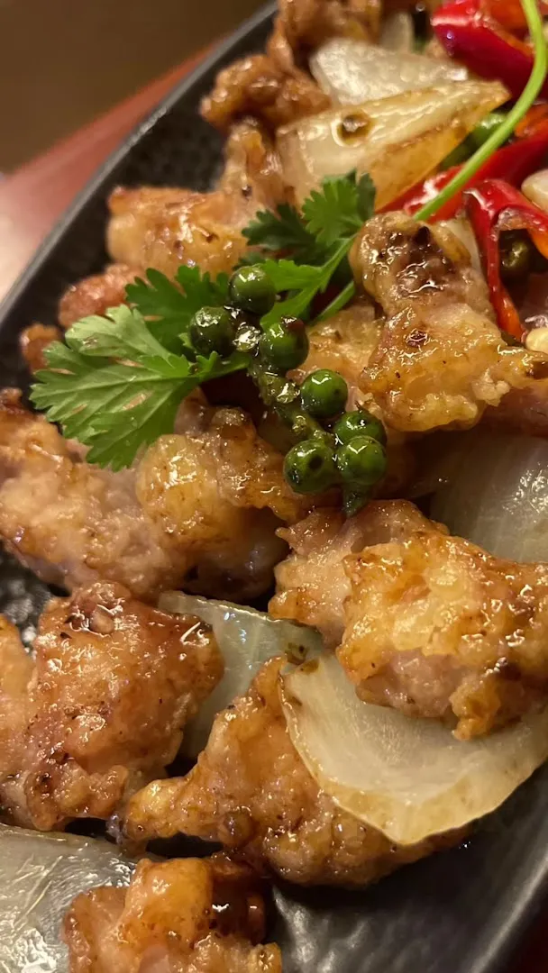 Món thịt chiên giòn phủ tiêu xanh, hành tây và ớt đỏ.