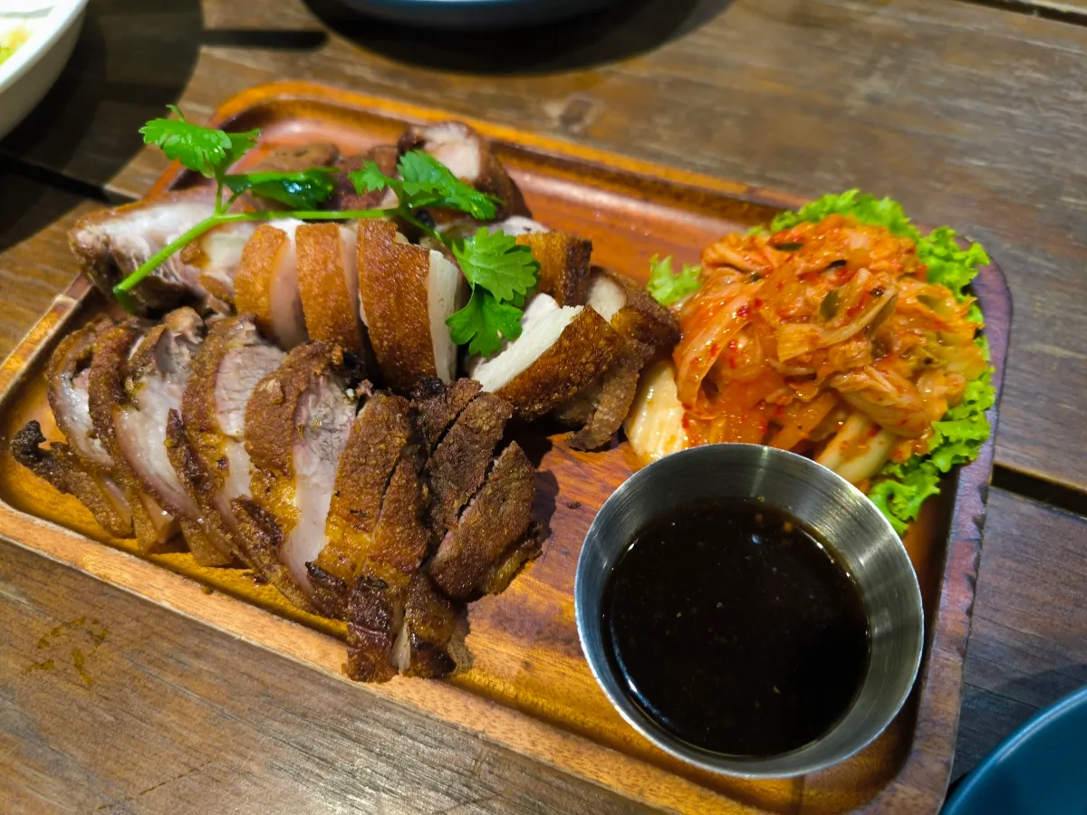 Đĩa thịt quay cắt lát ăn kèm kim chi, rau xanh và nước chấm.