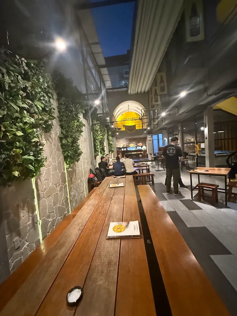Không gian bên trong Steersman Brewery với bàn ghỗ dài, quầy bar và khu vực khách ngồi.