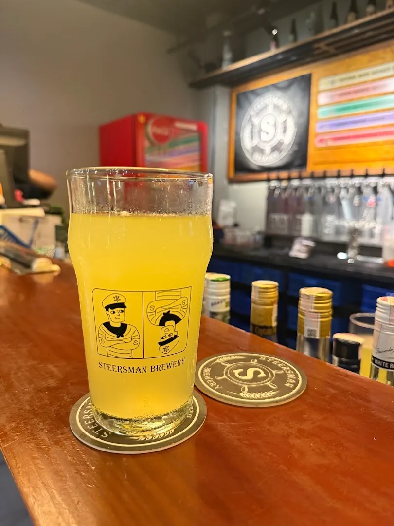Ly bia Steersman Brewery đặt trên quầy bar, phía sau là khu vực vòi rót bia.