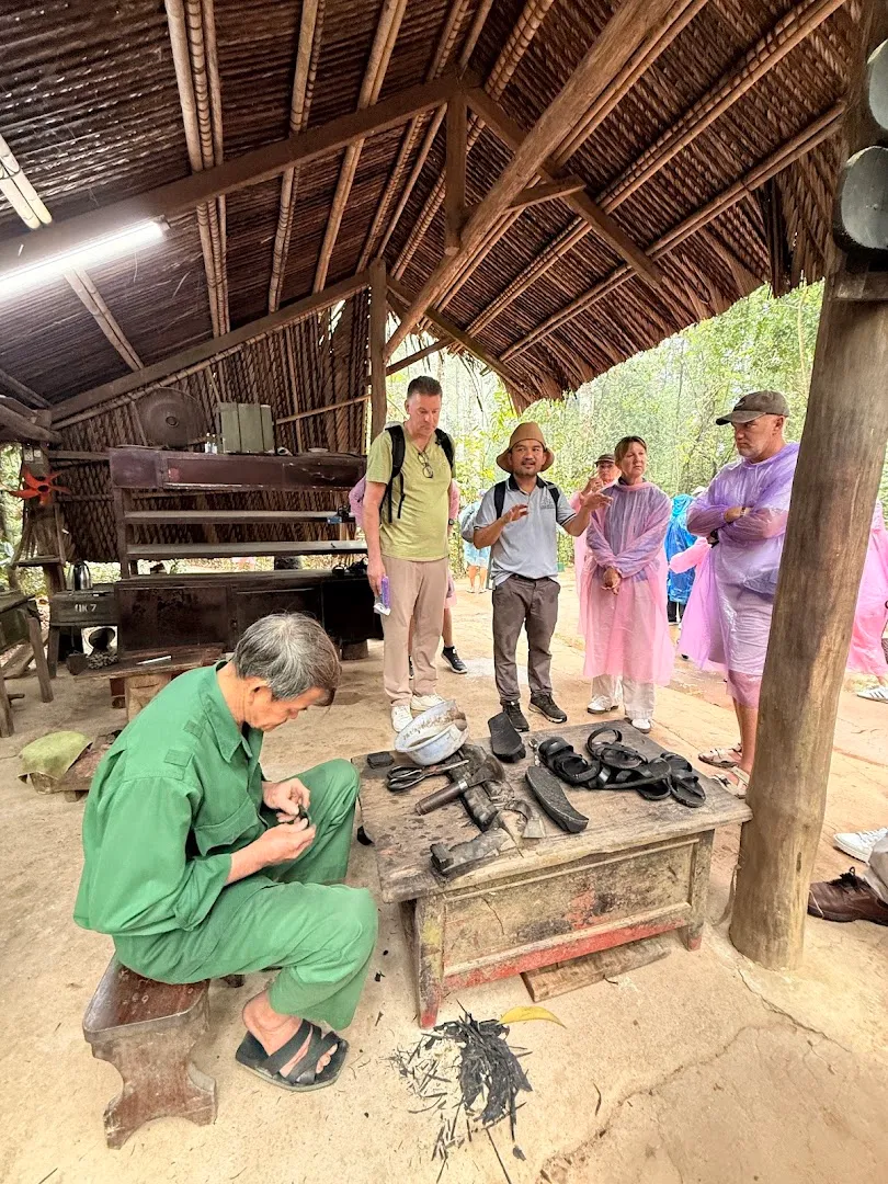Cảnh thợ thủ công làm việc trong một chòi mái lá trước nhóm du khách.