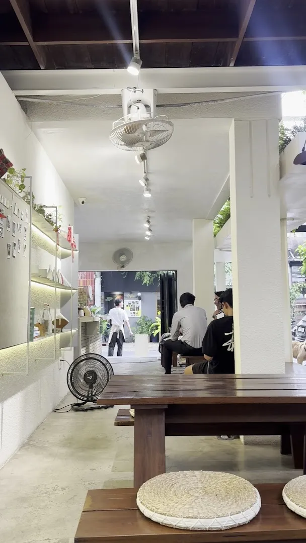 Không gian bên trong quán với bàn ghế gỗ, kệ trưng bày và khu vực ngồi chờ.