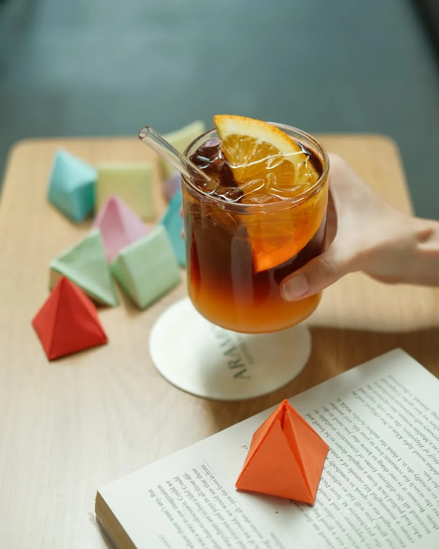Ly cà phê đá trang trí lát cam trên bàn cùng sách và các mô hình giấy màu.