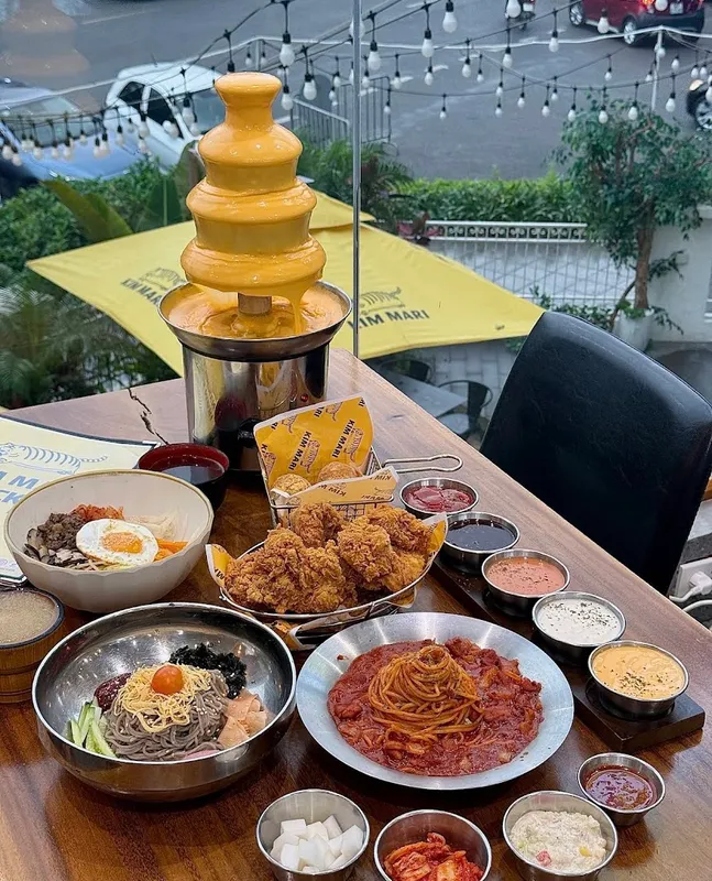 Bàn ăn với gà rán, mì, cơm và tháp phô mai trong không gian ngoài trời.
