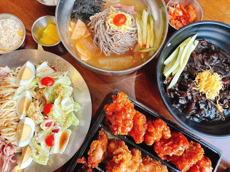 Các món gà chiên sốt, mì lạnh và salad được bày trên bàn.