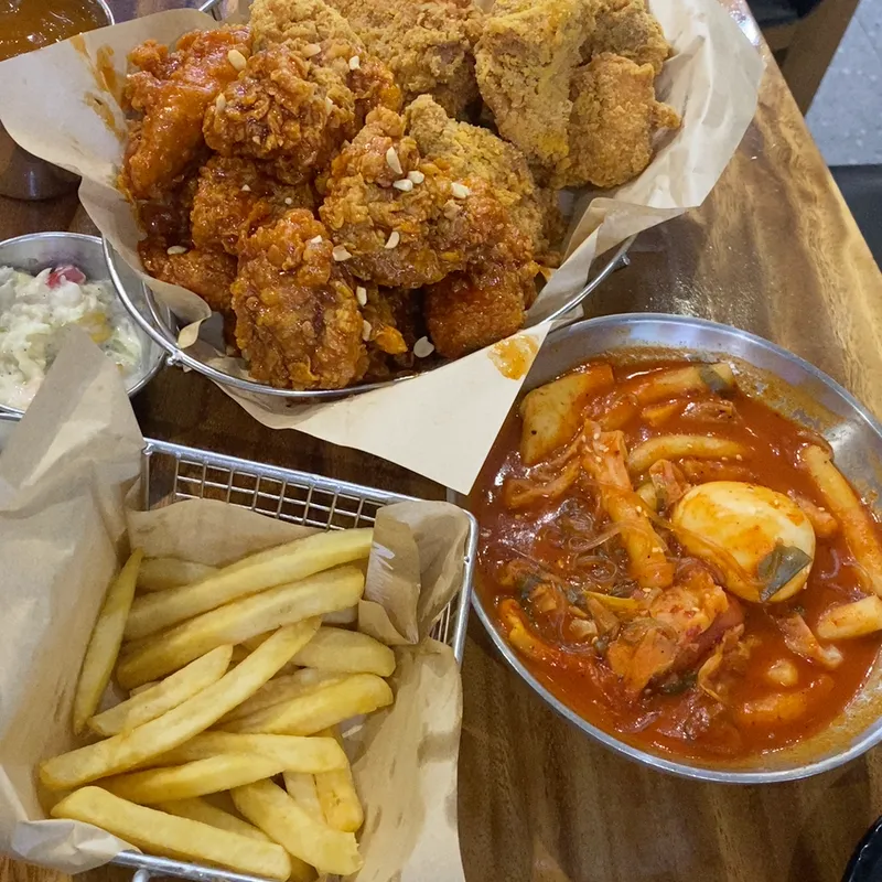 Gà rán sốt, khoai tây chiên và tokbokki được bày trên bàn.