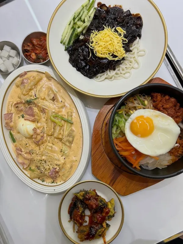 Các món ăn Hàn Quốc được bày biện trên bàn, gồm mì trộn, cơm trộn và các món ăn kèm.