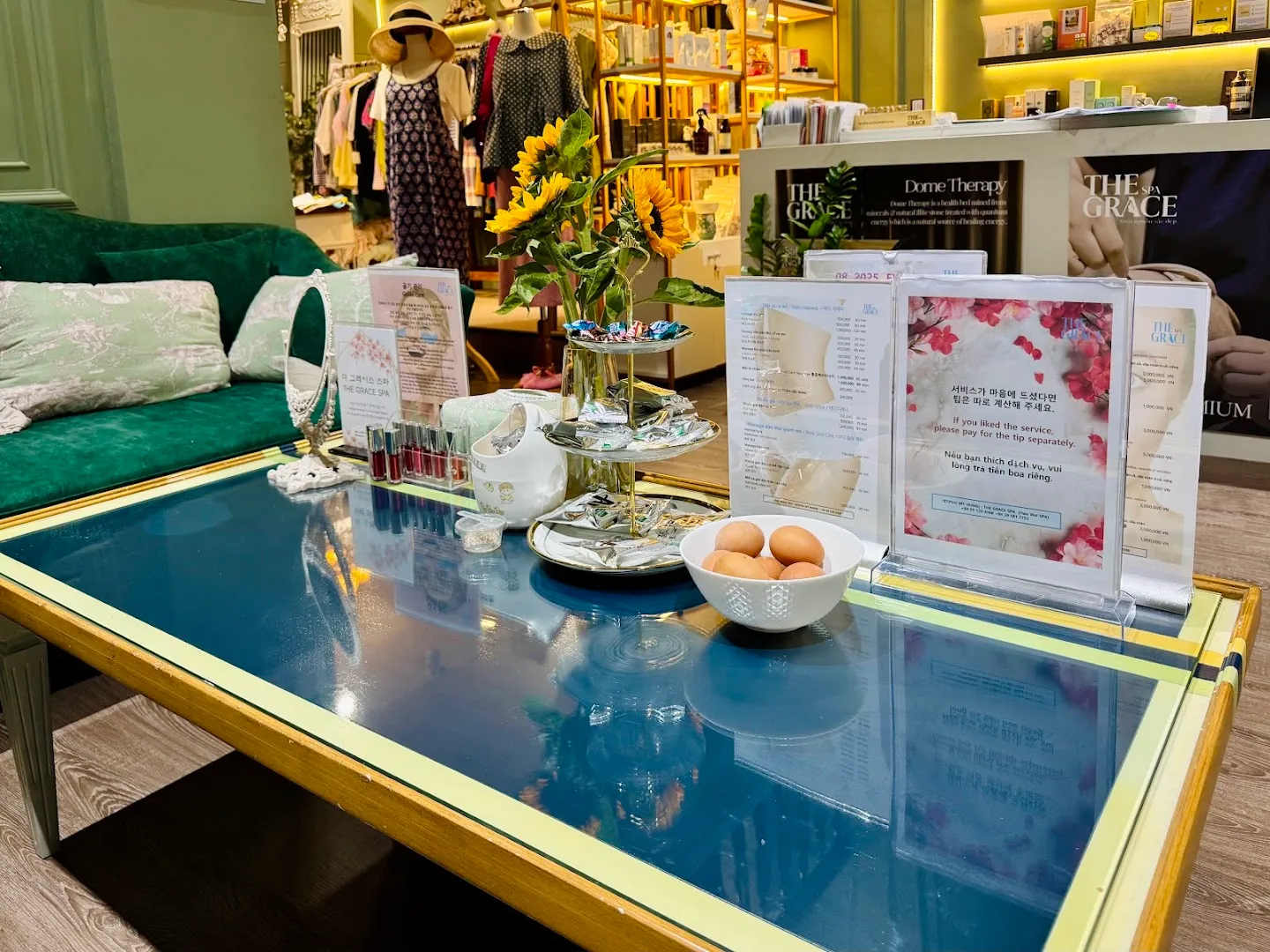 Không gian tiếp đón với bàn trà, hoa tươi và bảng dịch vụ của spa.