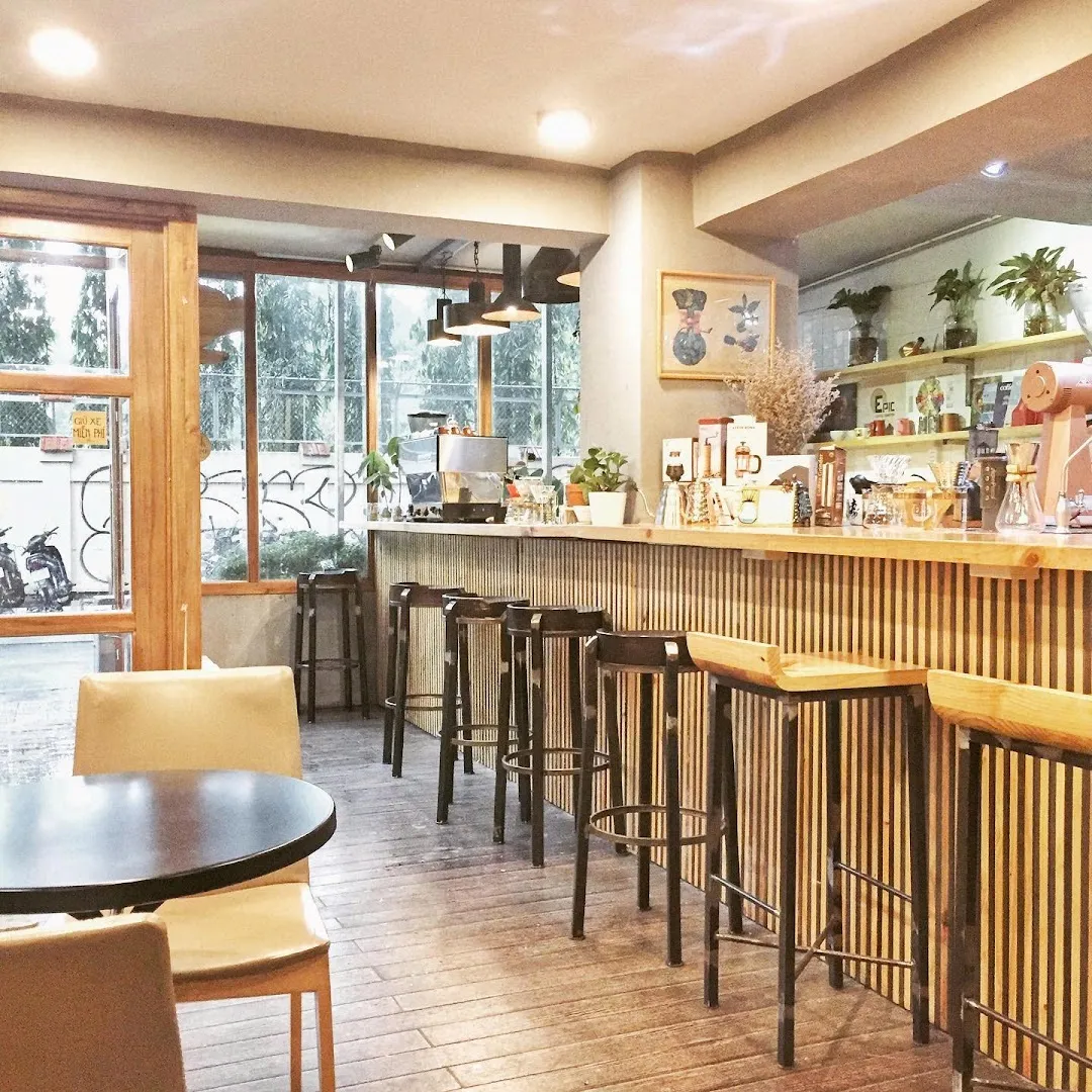 Không gian bên trong quán cà phê với quầy pha chế, bàn ghế và khu vực bar.