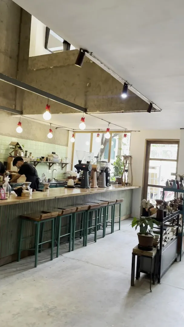 Không gian quán cà phê với quầy pha chế, máy pha cà phê và ghế bar.